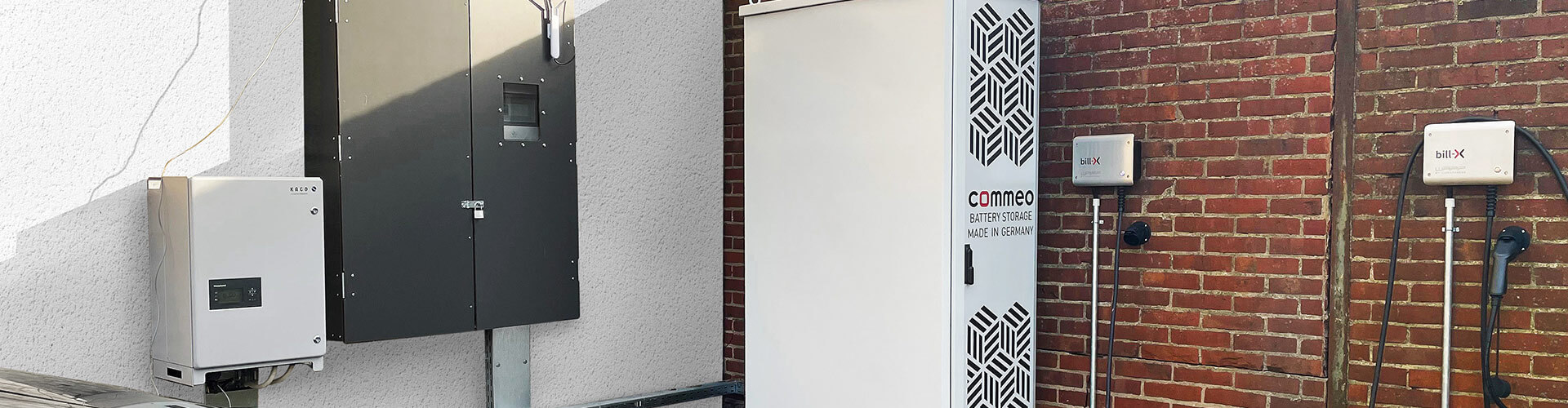 Das Bild präsentiert einen Commeo Batteriespeicher im Außenbereich der Firma bill-x GmbH. Deutlich sichtbar ist ein E-Auto, das gerade von diesem Speicher geladen wird.
